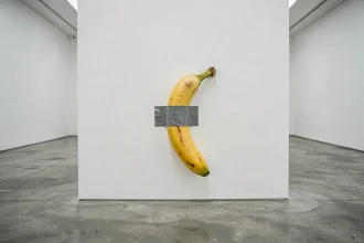 Une banane fixée avec du ruban adhésif gris sur un mur blanc de galerie d'art contemporain, évoquant l'œuvre Comedian de Maurizio Cattelan